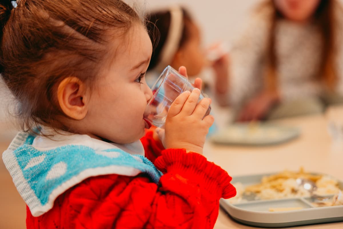 Enfant qui boit dans un verre à la cantine de la crèche