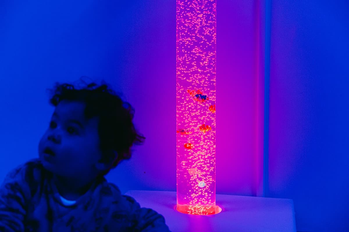 Enfant émerveillé par la colonne à bulles lumineuse de la salle sensorielle